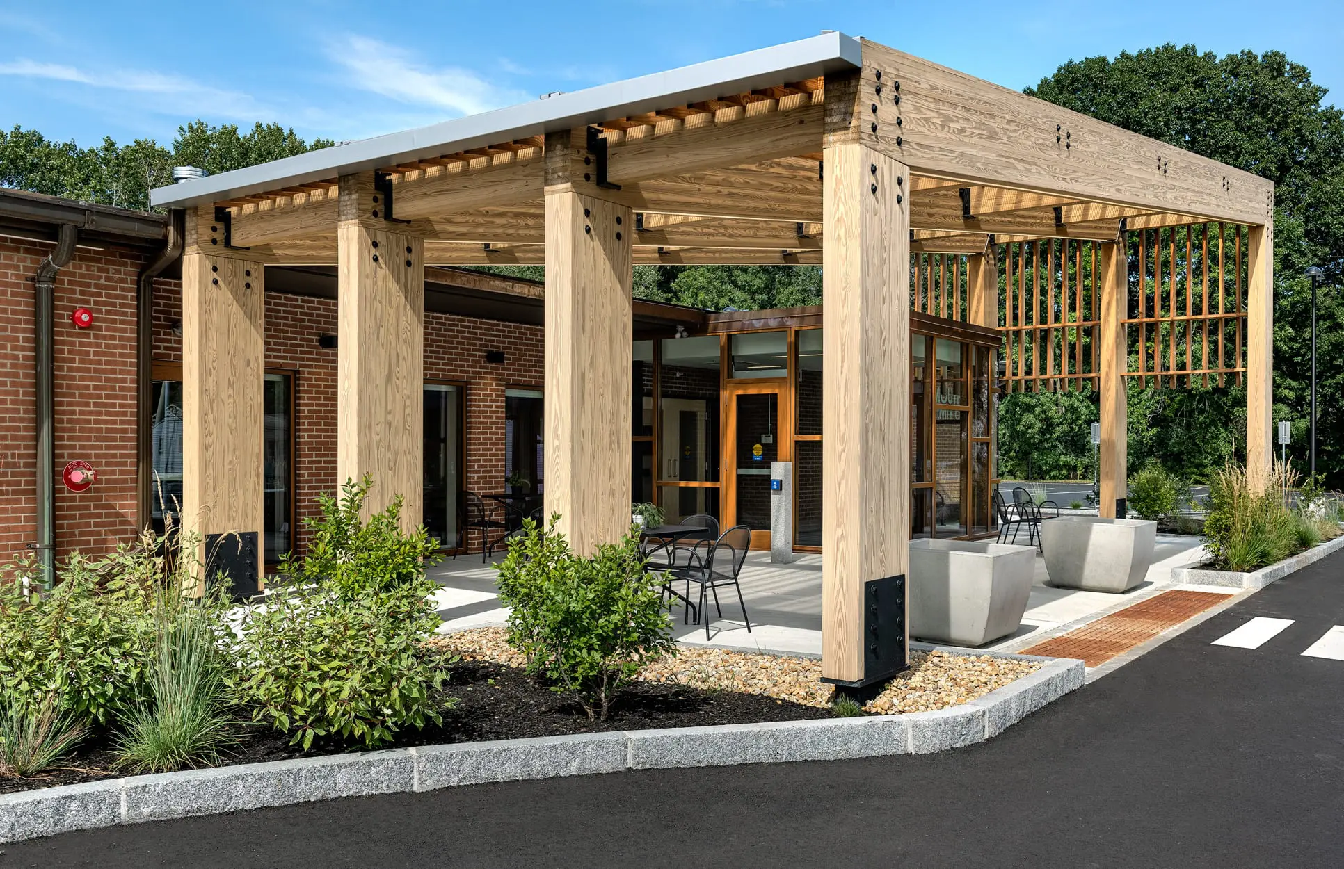 Wooden pergola in front of a brick building.