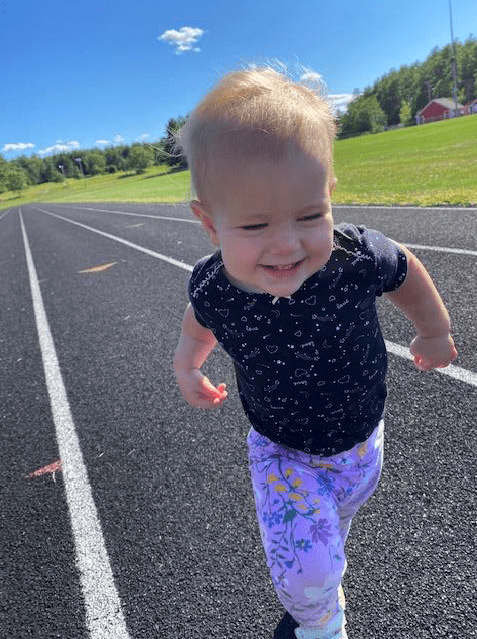 Toddler walking on a track outside.