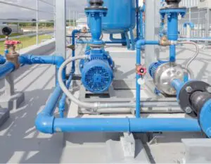 Screenshot Blue industrial water pumps and pipelines installed on a concrete platform outdoors, with several valves and connections visible; part of a water treatment or supply facility.