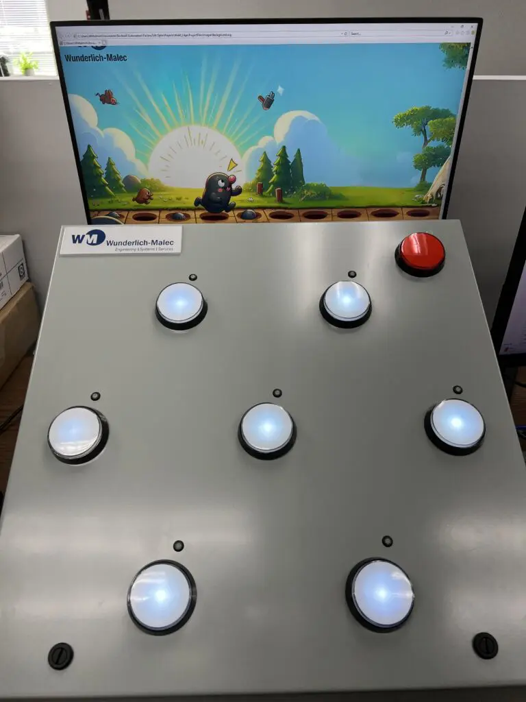 A whac-a-mole game interface with a monitor displaying cartoon moles and a gray control panel featuring seven illuminated buttons and one large red button. The panel is labeled "Wunderlich-Malec.