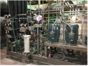Picture1 An industrial setup featuring metal pipes, gauges, valves, control panels, and two large dark green mechanical units, all mounted on a metal frame in a factory or plant setting.