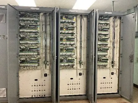 Three open electrical control panels reveal rows of wires, circuit boards, and connectors organized inside each metal cabinet, all standing side by side in an industrial or technical room.