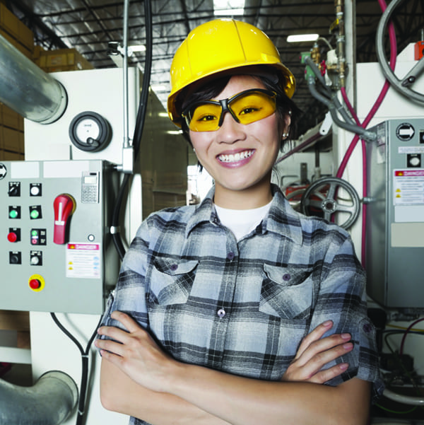 Portrait of female industrial worker smiling while standing in factory with machines in background