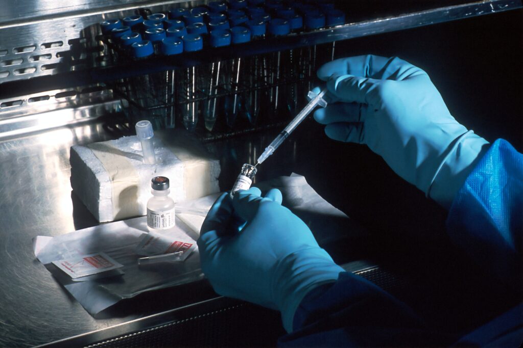 Close up of person wearing gloves to injects substance into test tube.