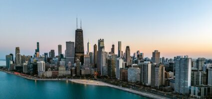 Aerial view of Chicago’s downtown skyline at sunset, with tall skyscrapers, including the John Hancock Center, along Lake Michigan’s waterfront. The sky is clear with soft evening light.