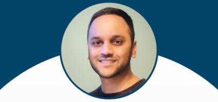 A smiling man with short dark hair and a trimmed beard, wearing a dark shirt, is shown in a circular frame against a blue and white background.