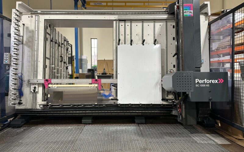 IMG_6119 A large industrial CNC machine, labeled "Perforex BC 1001 HS," stands in a factory. The machine is equipped with metal components, hoses, and a white panel being worked on. The area is clean and well-lit.