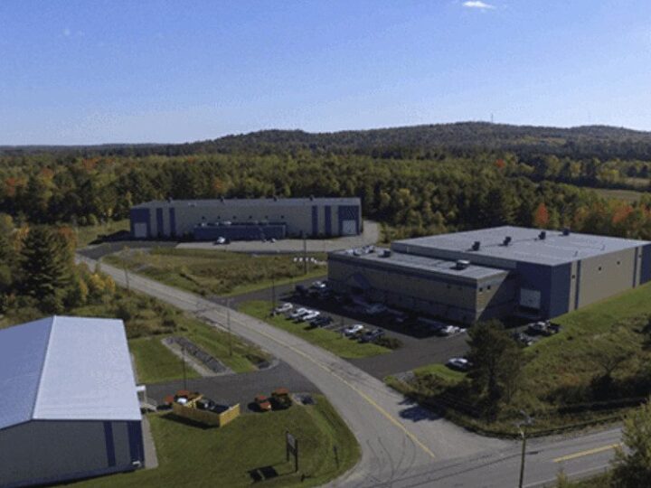 baldwin-florida-facility-1024x644 Aerial view of an industrial complex with three large gray buildings surrounded by trees, parked cars, and intersecting roads under a clear blue sky.